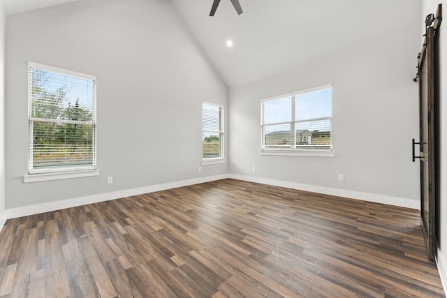 empty room featuring dark wood-type flooring, ceiling fan, a barn door, and a healthy amount of sunlight