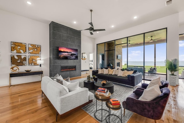 living room with a tiled fireplace, ceiling fan, light hardwood / wood-style flooring, and a water view