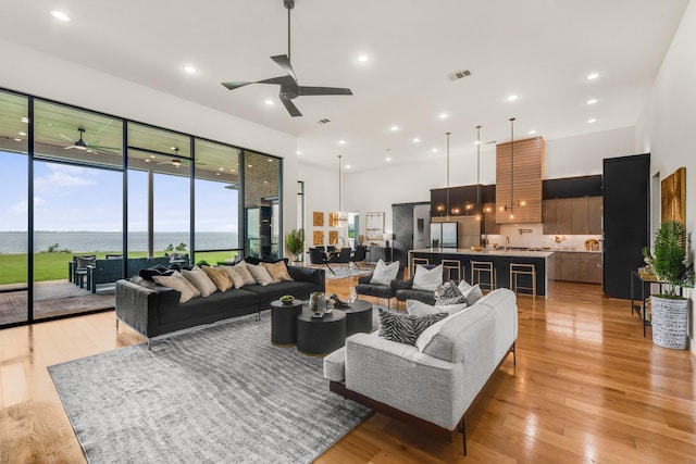 living room with ceiling fan, a water view, and light wood-type flooring