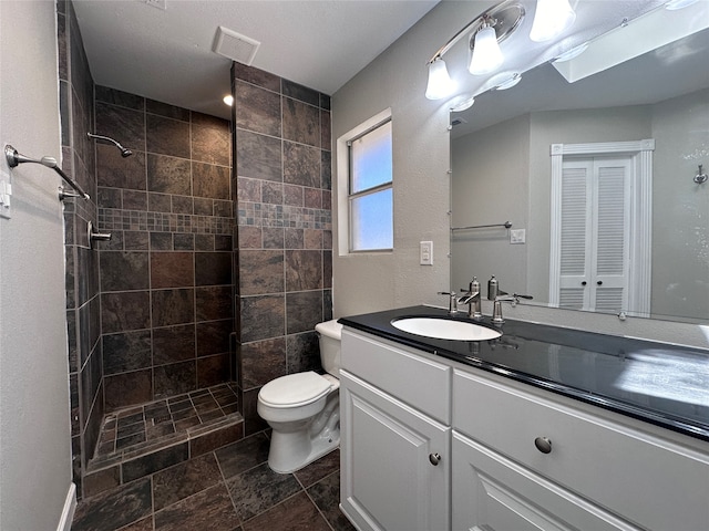 bathroom with a tile shower, vanity, and toilet