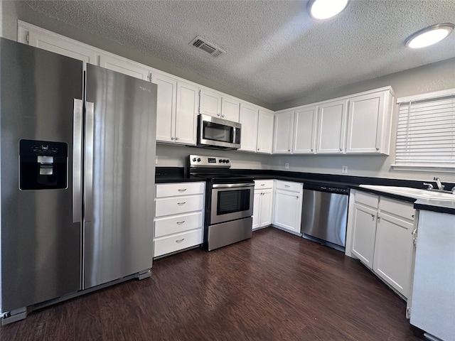 kitchen featuring appliances with stainless steel finishes, white cabinetry, dark wood-type flooring, a textured ceiling, and sink