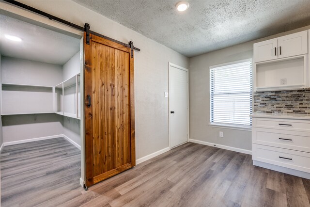 interior space with a barn door, baseboards, light wood-type flooring, and a textured ceiling