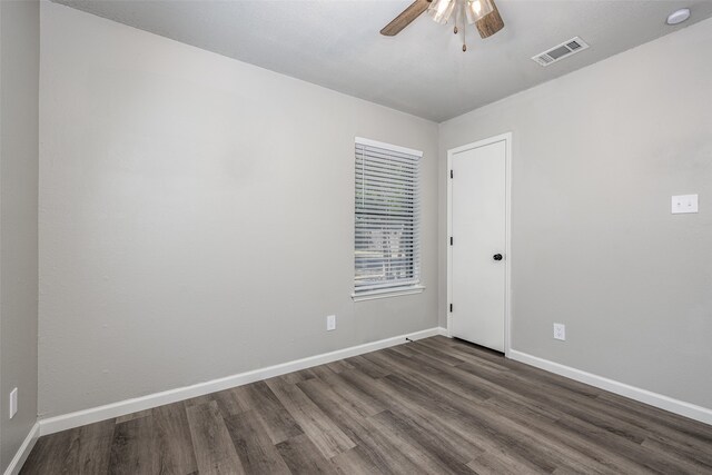 empty room with dark wood-style floors, visible vents, ceiling fan, and baseboards