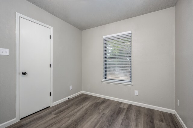 spare room featuring baseboards, dark wood-type flooring, and a textured ceiling