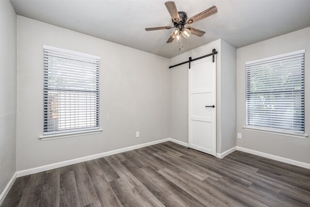 unfurnished bedroom featuring a barn door, baseboards, and dark wood-style floors