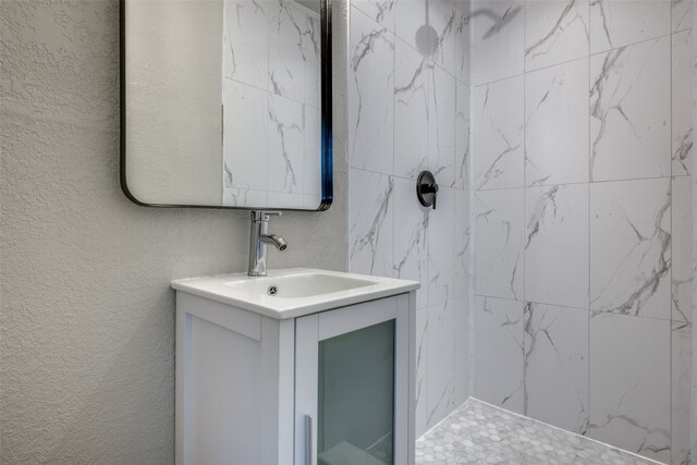 full bathroom featuring vanity, a textured wall, and tiled shower