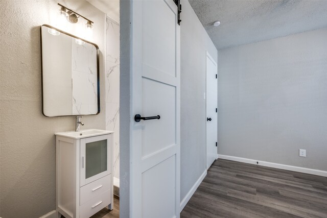 bathroom with a textured ceiling, vanity, baseboards, and wood finished floors