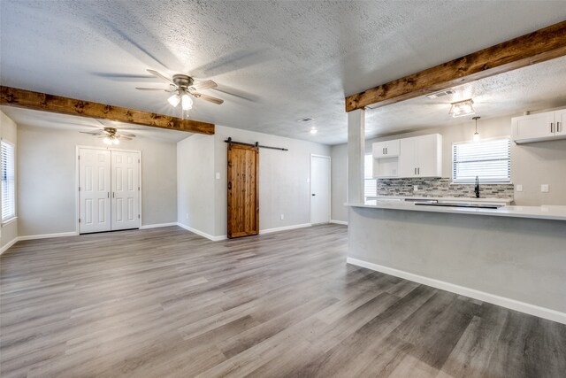 unfurnished living room with baseboards, a barn door, beam ceiling, light wood-style flooring, and a textured ceiling