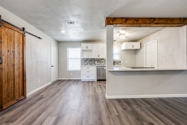 kitchen with visible vents, backsplash, a barn door, white cabinets, and dishwasher