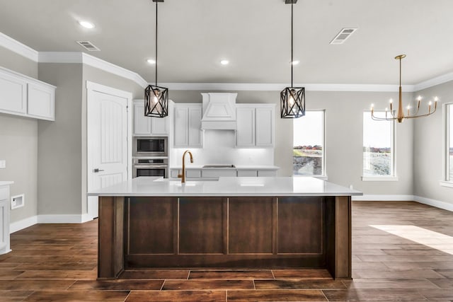 kitchen with pendant lighting, stainless steel appliances, a large island with sink, and dark wood-type flooring