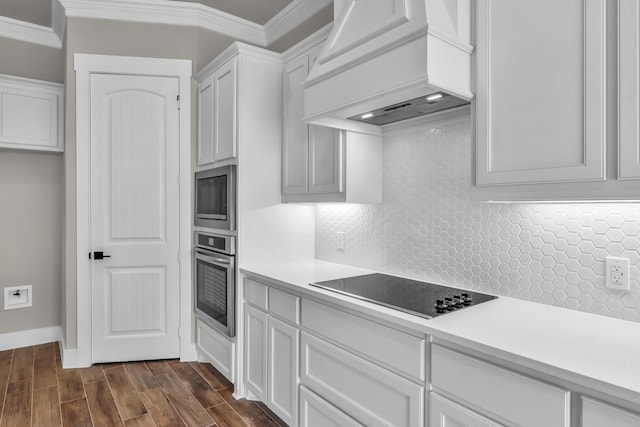 kitchen featuring custom exhaust hood, white cabinets, ornamental molding, appliances with stainless steel finishes, and dark hardwood / wood-style flooring