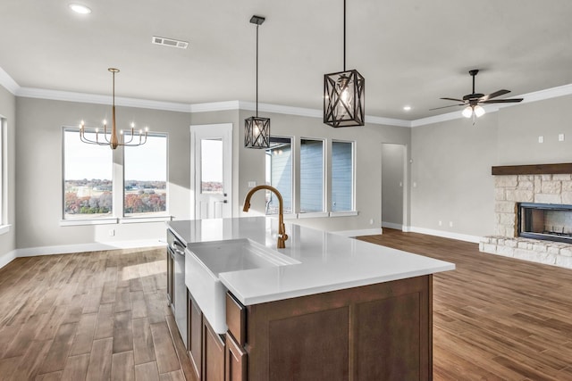 kitchen with wood-type flooring, decorative light fixtures, a kitchen island with sink, a fireplace, and ceiling fan with notable chandelier