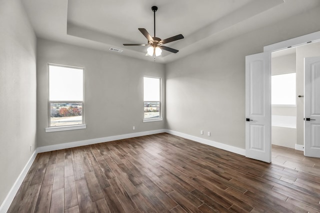 unfurnished room featuring a tray ceiling, ceiling fan, and dark wood-type flooring