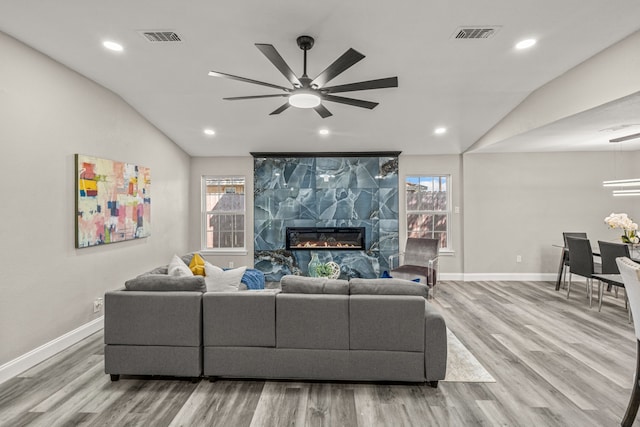 living room featuring ceiling fan, light wood-type flooring, vaulted ceiling, and a tile fireplace