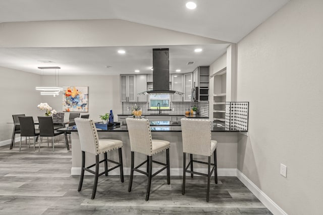 kitchen featuring lofted ceiling, kitchen peninsula, tasteful backsplash, island exhaust hood, and hardwood / wood-style flooring