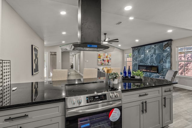 kitchen featuring light hardwood / wood-style floors, stainless steel electric stove, a fireplace, ceiling fan, and dark stone counters