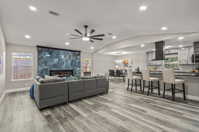 living room with light wood-type flooring, lofted ceiling, a tiled fireplace, and ceiling fan