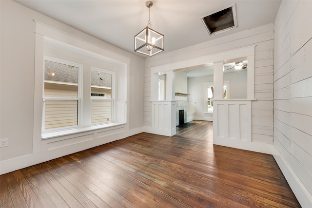 unfurnished dining area featuring ceiling fan with notable chandelier, dark hardwood / wood-style flooring, wooden walls, and plenty of natural light