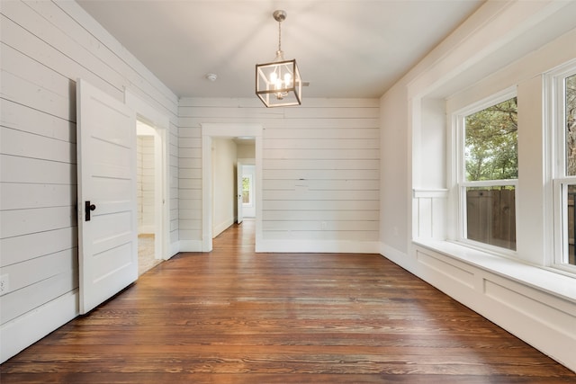 unfurnished dining area with wood walls, dark hardwood / wood-style floors, and a chandelier