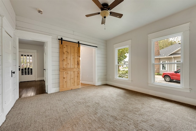 unfurnished bedroom with a barn door, ceiling fan, multiple windows, and carpet