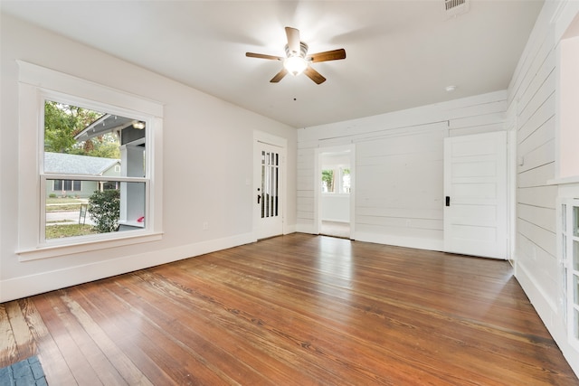 interior space with hardwood / wood-style floors, wood walls, and ceiling fan