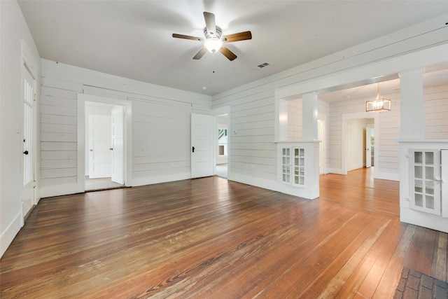 unfurnished living room with hardwood / wood-style floors, ceiling fan, and wooden walls