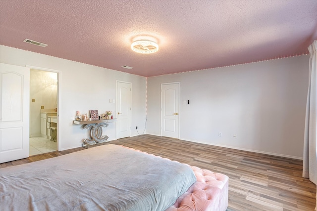 bedroom with a textured ceiling, connected bathroom, and light hardwood / wood-style floors