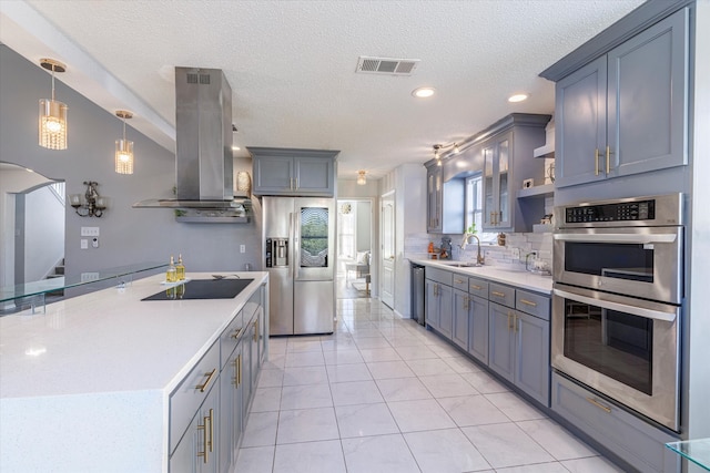 kitchen with light tile patterned floors, stainless steel appliances, decorative light fixtures, sink, and wall chimney range hood