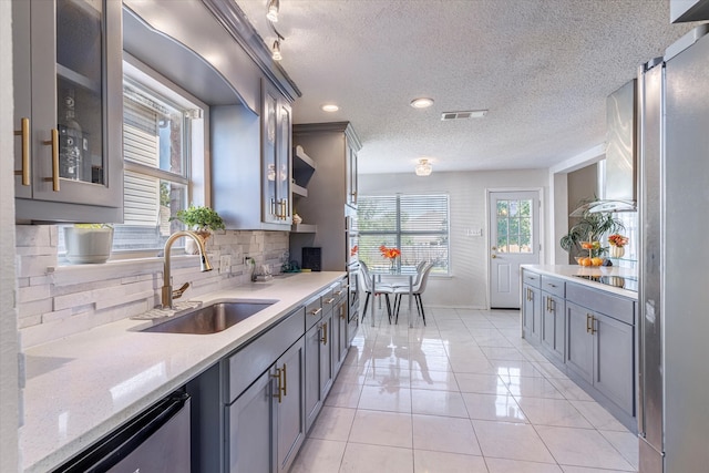 kitchen featuring appliances with stainless steel finishes, light tile patterned flooring, light stone counters, backsplash, and sink