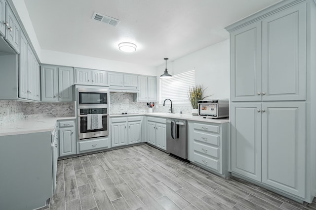 kitchen featuring gray cabinets, light wood-type flooring, pendant lighting, tasteful backsplash, and appliances with stainless steel finishes