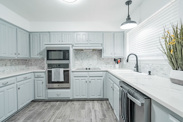 kitchen featuring hanging light fixtures, sink, light hardwood / wood-style flooring, stainless steel appliances, and decorative backsplash