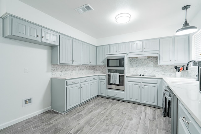 kitchen featuring light wood-type flooring, stainless steel appliances, sink, pendant lighting, and backsplash