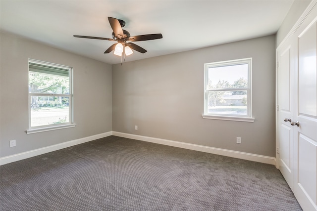 unfurnished room with dark colored carpet, ceiling fan, and a healthy amount of sunlight