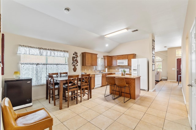 kitchen with decorative backsplash, vaulted ceiling, white appliances, a kitchen island, and a breakfast bar area