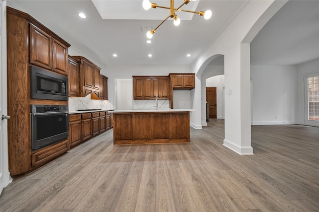 kitchen featuring stainless steel oven, a kitchen island, black microwave, and light wood-type flooring