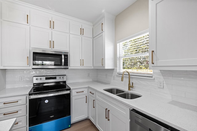 kitchen with light stone countertops, backsplash, stainless steel appliances, sink, and white cabinetry