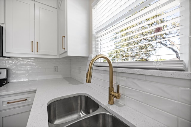 kitchen featuring backsplash, light stone counters, sink, and white cabinetry