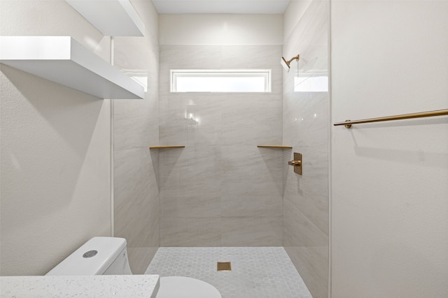 bathroom with a tile shower and toilet