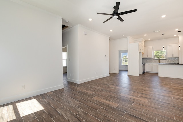 unfurnished living room with ceiling fan, sink, crown molding, and dark hardwood / wood-style flooring