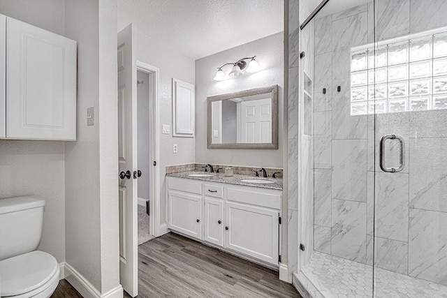 bathroom with walk in shower, vanity, a textured ceiling, wood-type flooring, and toilet