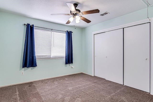 unfurnished bedroom with ceiling fan, dark carpet, a textured ceiling, and a closet