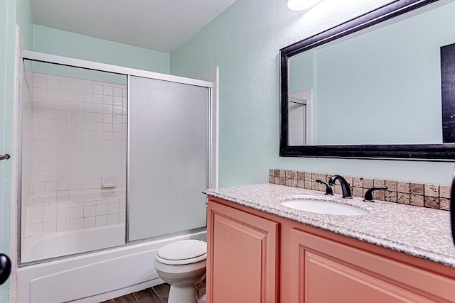 full bathroom featuring shower / bath combination with glass door, hardwood / wood-style floors, vanity, and toilet