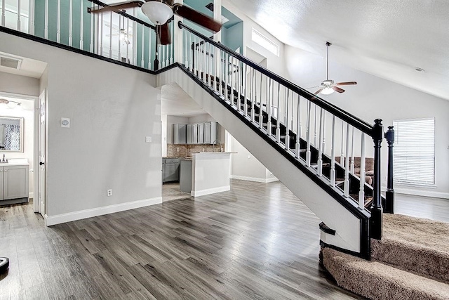 staircase with ceiling fan, high vaulted ceiling, a healthy amount of sunlight, and hardwood / wood-style flooring