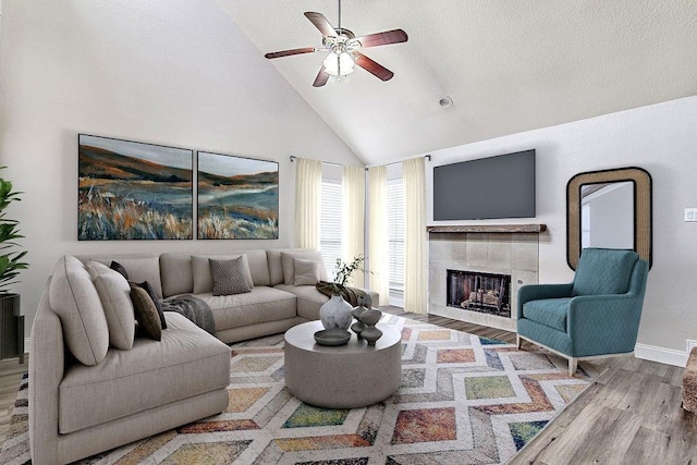 living room featuring high vaulted ceiling, ceiling fan, a textured ceiling, a fireplace, and light hardwood / wood-style floors