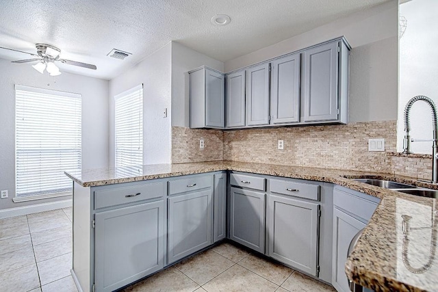 kitchen with a textured ceiling, light stone countertops, kitchen peninsula, and sink