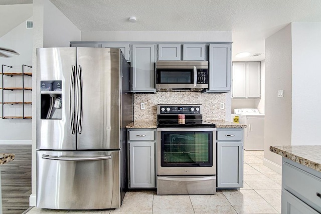 kitchen with gray cabinets, washer and dryer, light tile patterned floors, and stainless steel appliances