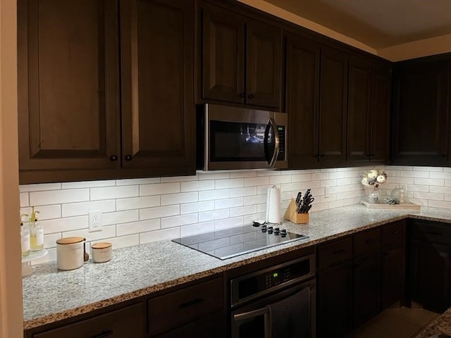 kitchen with dark brown cabinetry, stainless steel appliances, light stone counters, and backsplash