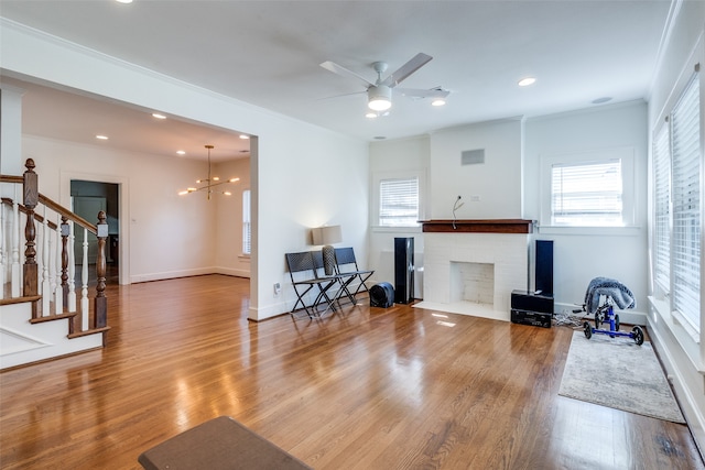 living room with a fireplace, hardwood / wood-style floors, ceiling fan with notable chandelier, and ornamental molding