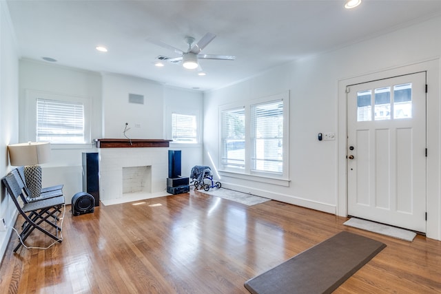 foyer entrance featuring hardwood / wood-style floors, plenty of natural light, crown molding, and a brick fireplace