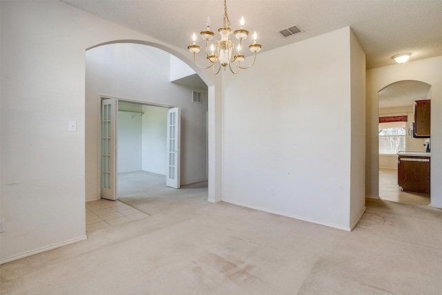 unfurnished room with light colored carpet, a notable chandelier, and a textured ceiling